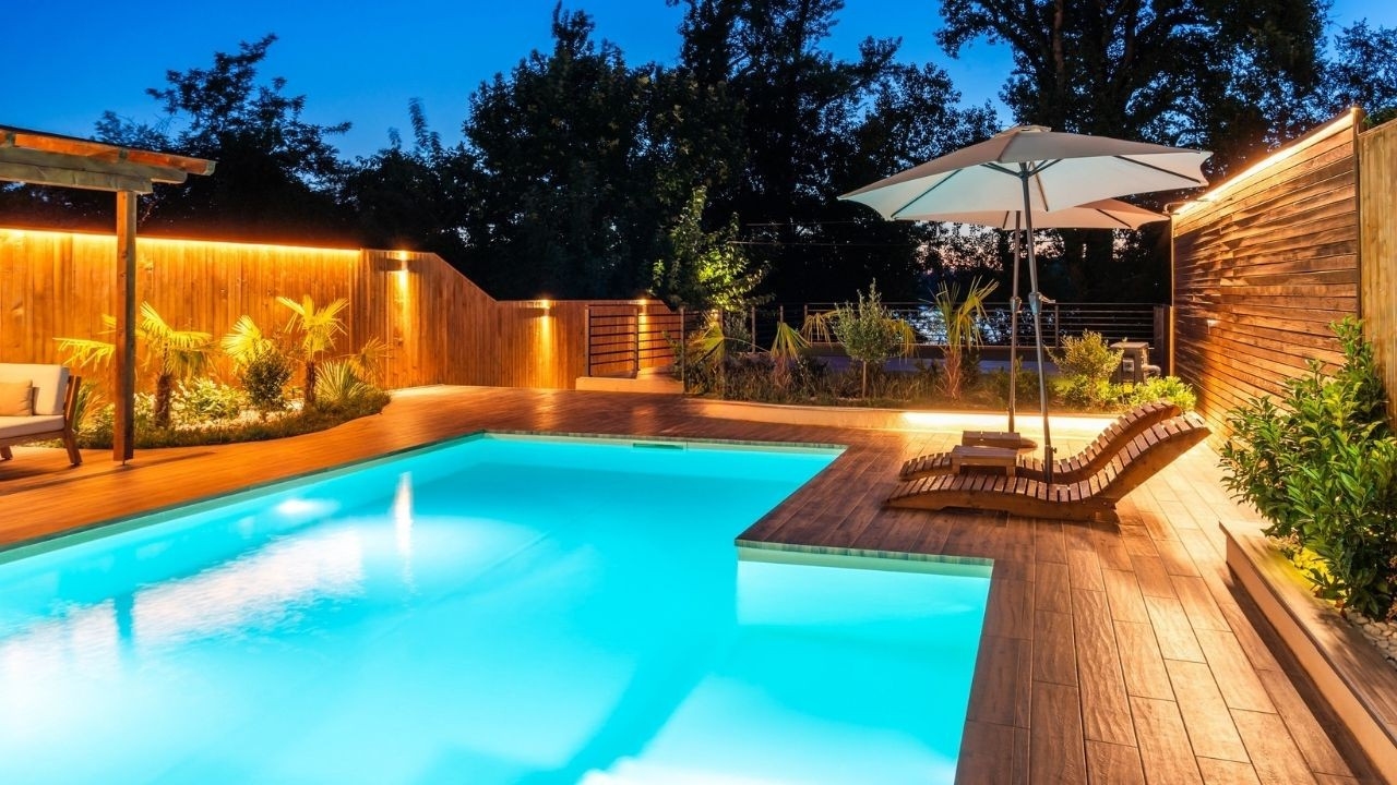 Resort-style infinity swimming pool illuminated at night with lounge chairs